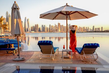 Beautiful beach in Dubai with a lady in red and white hat, 2 sun chairs and an umbrella.