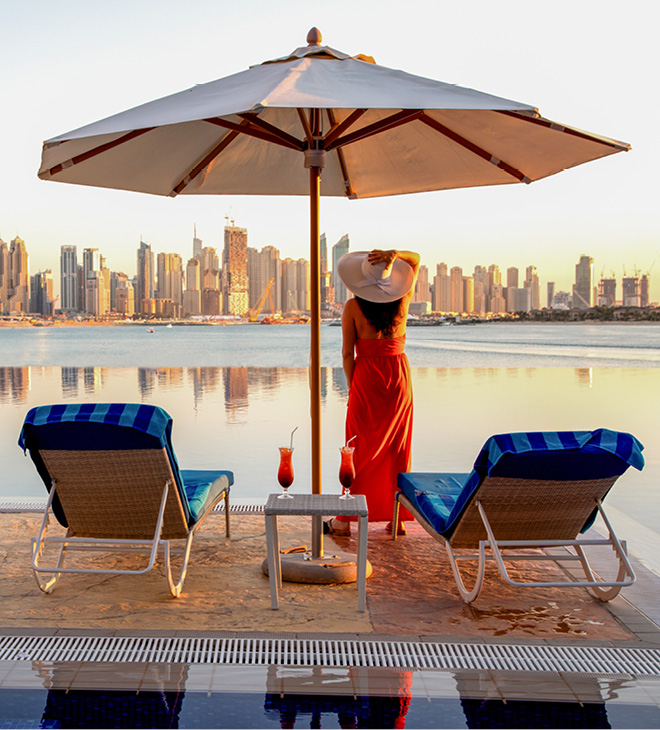 Beautiful beach in Dubai with a lady in red and white hat, 2 sun chairs and an umbrella.